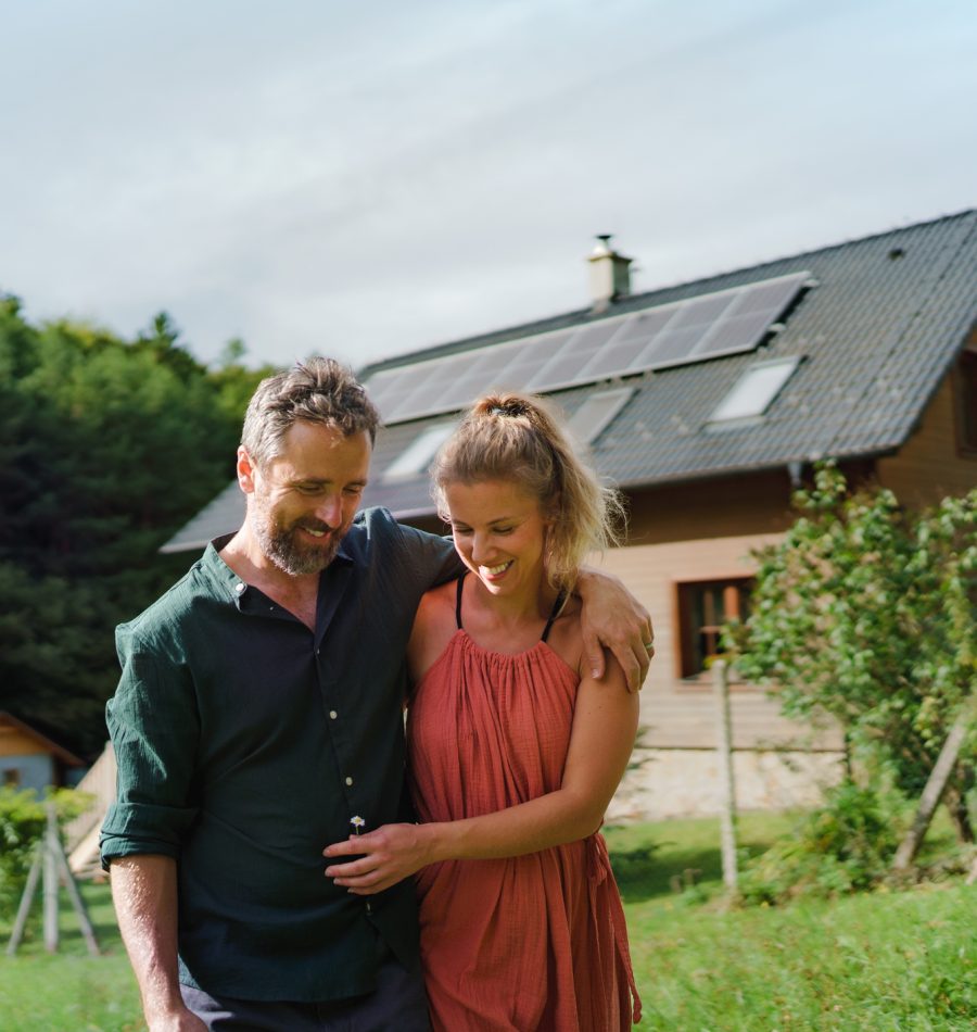 Happy couple standying near their house with a solar panels. Alternative energy, saving resources and sustainable lifestyle concept.