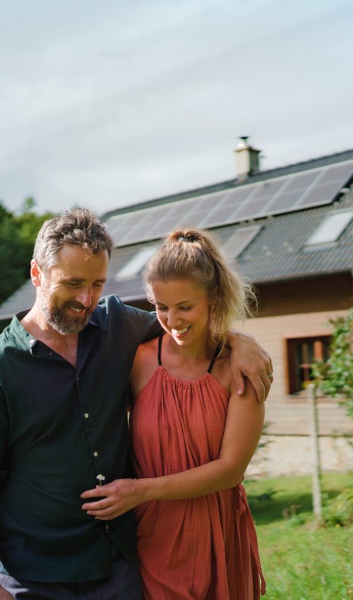 Happy couple standying near their house with a solar panels. Alternative energy, saving resources and sustainable lifestyle concept.